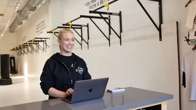 Woman works on her laptop at fitness studio front desk