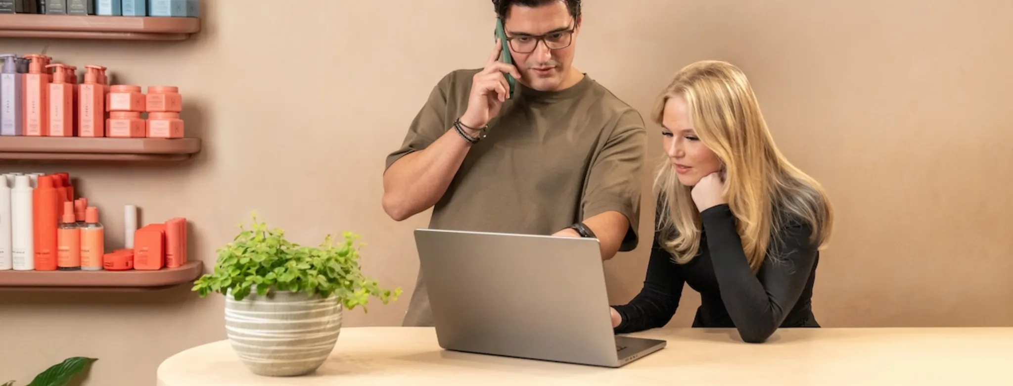 Two people using the computer at a salon's front desk.