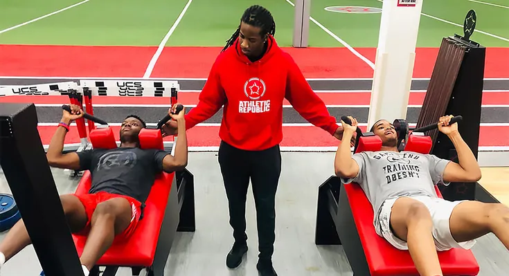 A trainer at Athletic Republic helping athletes with leg presses