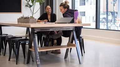Two women sit at desk discussing business