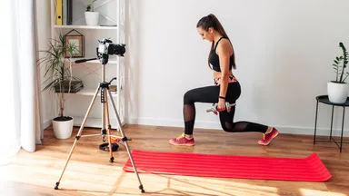 Fitness instructor filming a video workout at home in front of a camera on a tripod
