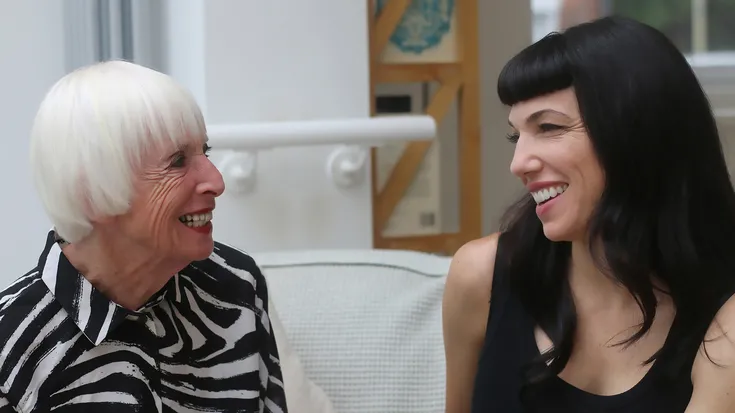 Esther Fairfax and Andrea Lucas talking on a white couch