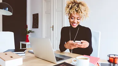 Person looking at phone while at desk with laptop