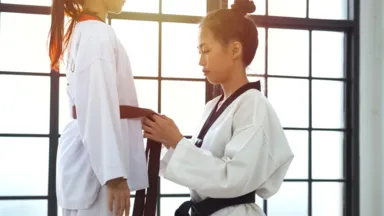 A martial arts instructor helps tie a student's black belt to prepare for Taekwondo