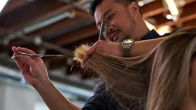 Man cutting blond woman's hair with scissors