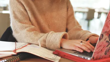 woman in tan sweater with a pink floral laptop